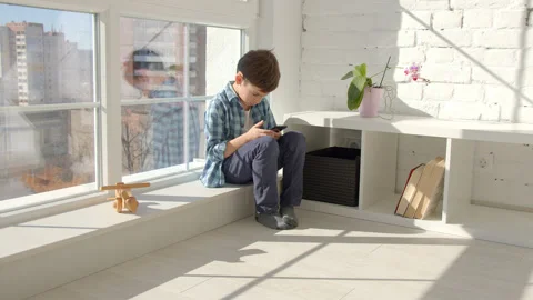 Boy sitting on windowsill, using mobile cell phone, watching video, playing game Stock Footage 171091532