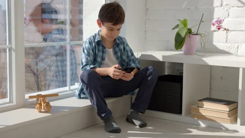 Boy sitting on windowsill, using mobile cell phone, watching video, playing game Stock Footage 171091608