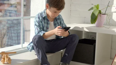 Boy sitting on windowsill, using mobile cell phone, watching video, playing game Stock Footage 171091942