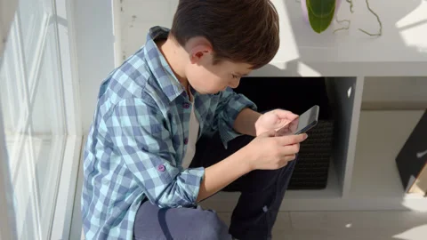 Boy sitting on windowsill, using mobile cell phone, watching video, playing game Stock Footage 171091991