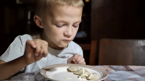 Boy six years old eating dumplings, sitting at table enjoying delicious food Stock Footage 285024572