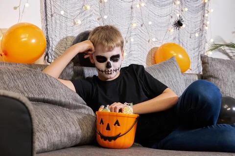 A boy in skeleton makeup pulls out candy from a Halloween party. Stock Photos