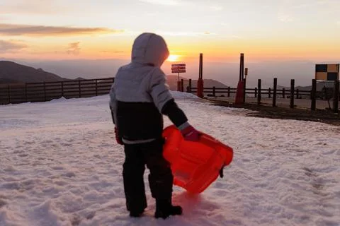 Boy with sled standing backlit at sunset in the snow Stock Photos