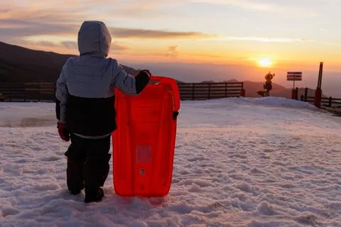 Boy with sled standing backlit at sunset in the snow Stock Photos