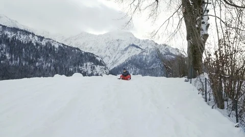 Boy sleds down a snowy hill with mountains in the background Stock Footage 121754054