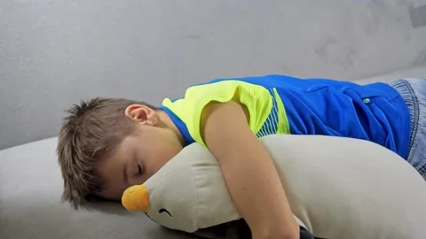 The boy is sleeping lying on the sofa with a soft toy. a penguin toy. gentle Stock Footage 168943047