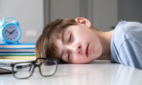 A boy is sleeping on a table with a clock and a stack of books Stock Photos
