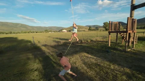 Boy slides on zipline as brother pulls him, camera pans to follow slow motion 스톡 동영상 248162129