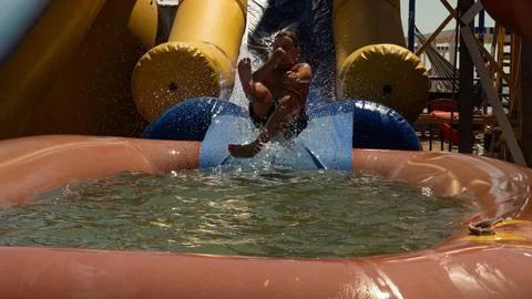 A boy sliding down an inflatable water slide falls into a pool of water causing Stock Photos