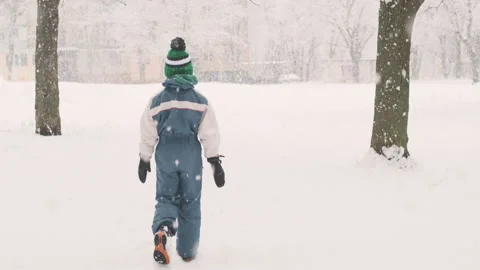 Boy slowly walks through snow-covered park during snowfall Video stock 211687679