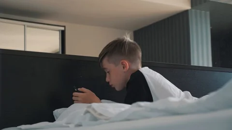 A boy with a smartphone is lying on the bed. The boy communicates with friends Video stock 94375133