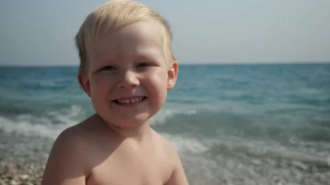 The boy smiles at the camera sitting on the seashore Stock Footage 220362895