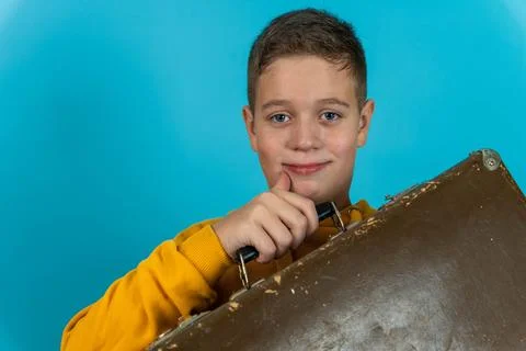 Boy smiles while holding a suitcase against a blue background at home Stock Photos