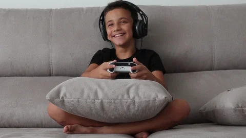 Boy smiling and having fun playing a video game with controllers on a couch. Stock Footage 114940230