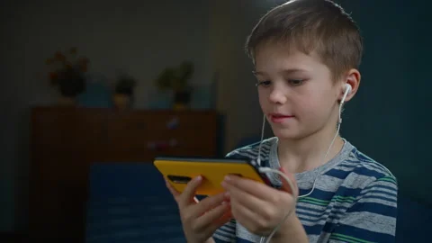 Boy Smiling While Watching Content on Phone with Headphones in Cozy Room Stock Footage 302842188