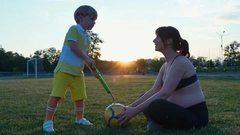 Boy soccer player pumps a ball with his pregnant mother in the stadium, at Stock Footage 197366296