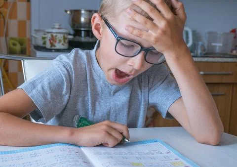 The boy solves math, does homework in the kitchen and yawns from boring tas.. Stock Photos