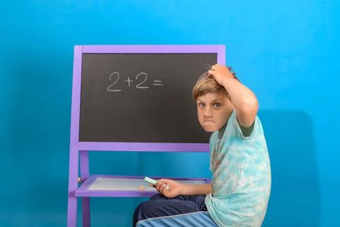The boy solves the math equation 2 + 2 written on the blackboard. The child s Stock Photos