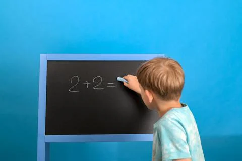 The boy solves the math equation 2 + 2 written on the blackboard. The child w Stock Photos