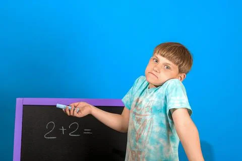 The boy solves the math equation 2 + 2 written on the blackboard. The child d Stock Photos