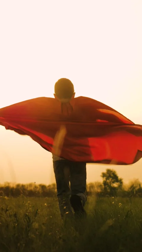 Boy son child superhero game running park field sunset grass victory red cloak Stock Footage 296708109