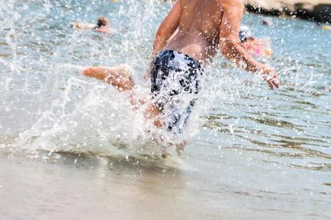 Boy splashing water while running into the sea Stock Photos