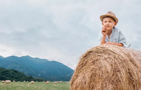 Boy in sraw hat lying on hay roll Stock Photos