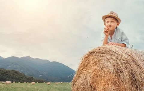 Boy in sraw hat lying on hay roll Stock Photos