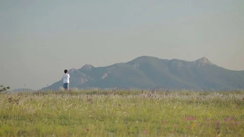 The boy is standing and looking at the mountains Stock Footage 76491282