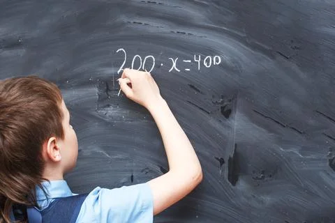 Boy standing back in front of school blackboard and writing. Schoolboy solves Stockfoto's