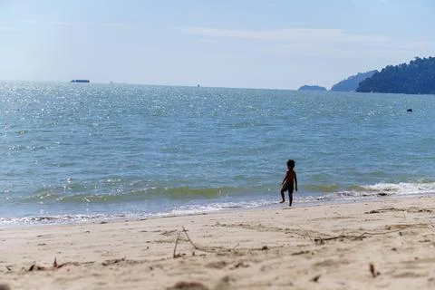 Boy standing on a beach looking at a large wave Stock Photos