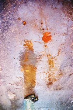 A boy standing in a blue jacket reflection in a frozen winter puddle Stock Photos