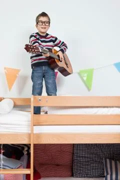 A boy standing on a bunk bed playing with a guitar Stock Photos