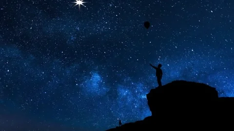 Boy standing on cliff with balloon flying away - Starry night Stock Footage 260114848