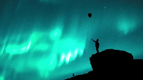 Boy standing on cliff with balloon flying away - northern lights Stock Footage 260114854