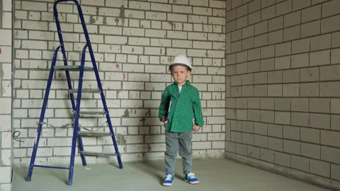 A boy is standing at a construction site in a white helmet and a green shirt Stock Footage 238477112