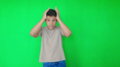 A boy is standing in front of a green wall with his head tilted Stock Footage 312356791