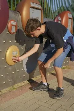 A boy is standing in front of a machine with a gold button Stock Photos