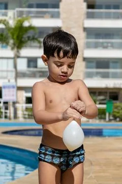 Boy standing in front of the pool playing with a water balloon. Stock Photos