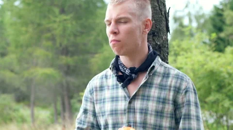 Boy standing next to the tree and eating tasty apple while looking to the camera Видео 67577680