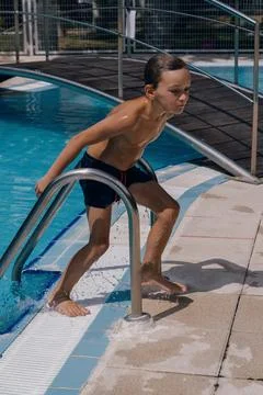 A boy is standing on a pool ladder and splashing water. Stock Photos