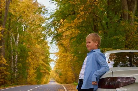Boy is standing on the side of the road next to the car Stock Photos