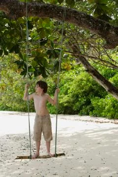 Boy standing on swing on beach Stock Photos