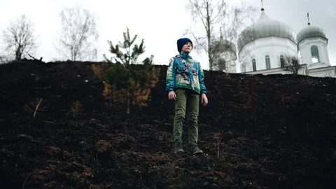 The boy stands on the burnt grass on a steep slope and looks ahead Stock Footage 128016617