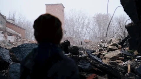 A boy stands in front of the ruins of destroyed houses. Snow is falling Stock Footage 126299982