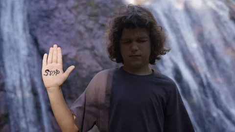 Boy stands sad and crying, in the shade, with his hand raised in the sun on Stock Footage 191461252