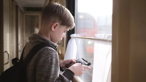 The boy stands at the train window with a tablet in his hands. Travel by train Stock-Footage 98629275