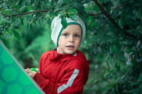 Boy stands under a tree and holds a green umbrella in his hands. Stock Photos