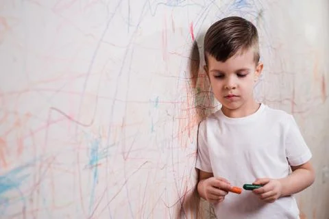 A boy stands at a wall painted by him with crayons in his hand. A child is en Stock Photos
