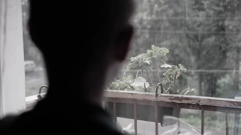 The boy stands at the window behind which there is a downpour Stock Footage 318384638